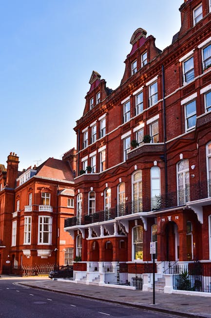 A rectangular white sign with black and red text is mounted on a brick wall, displaying 'Welcome to South Kensington SW7'. The sign is attached with four metal bolts, one in each corner. The wall behind the sign consists of reddish-brown bricks arranged in a running bond pattern with visible mortar joints. The lighting appears natural, illuminating the sign evenly, and the bricks have a textured surface. This signage is relevant to house removals and moving services in the South Kensington area, where [COMPANY_NAME] may assist with furniture transport and packing during a home relocation process.